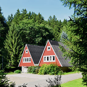 Bild einer roten Wanderhütte mit doppeltem Spitzdach im Wald.